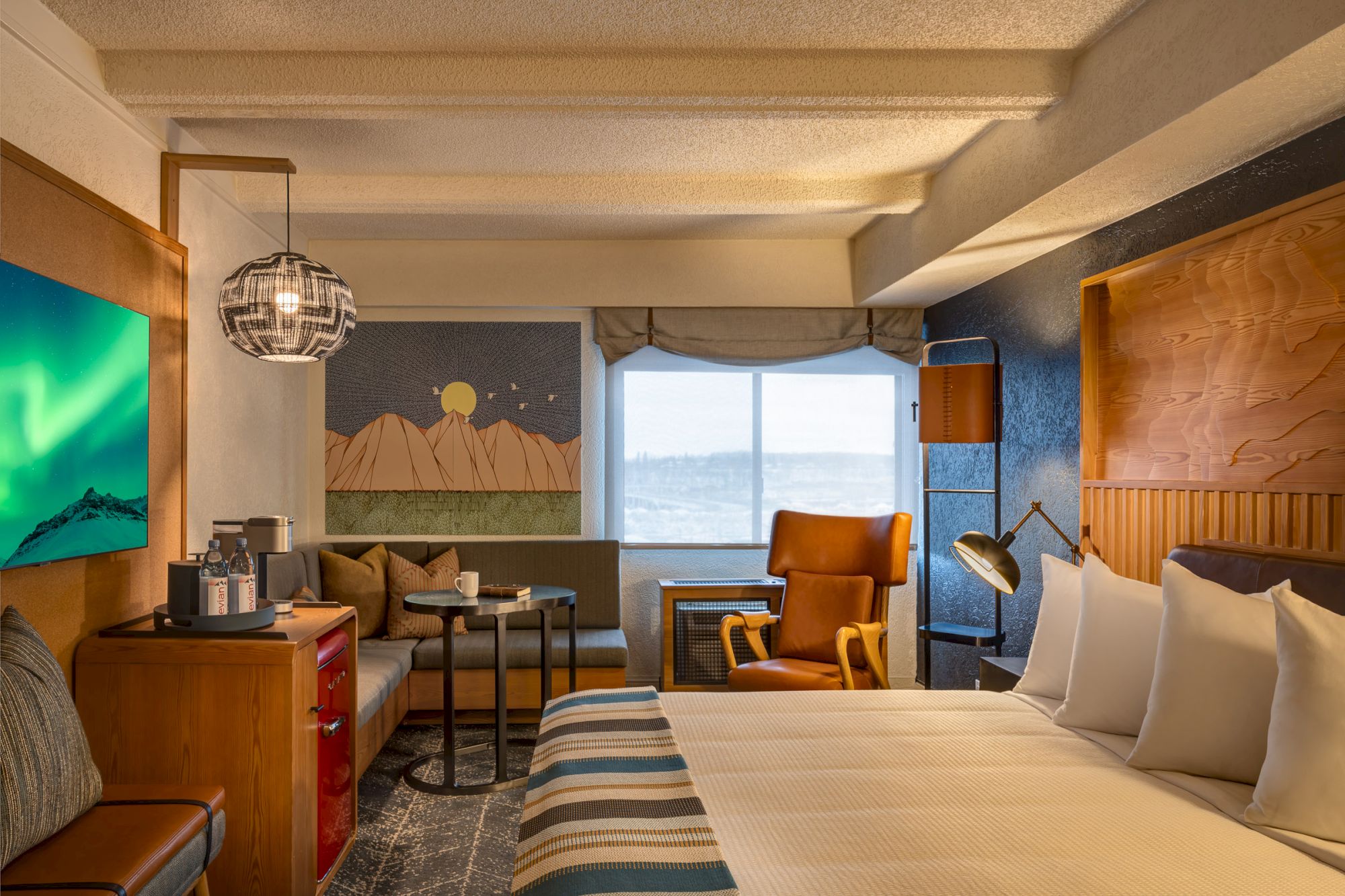 A well-decorated hotel room with a bed, seating area, large window, and mountain-themed wall art.