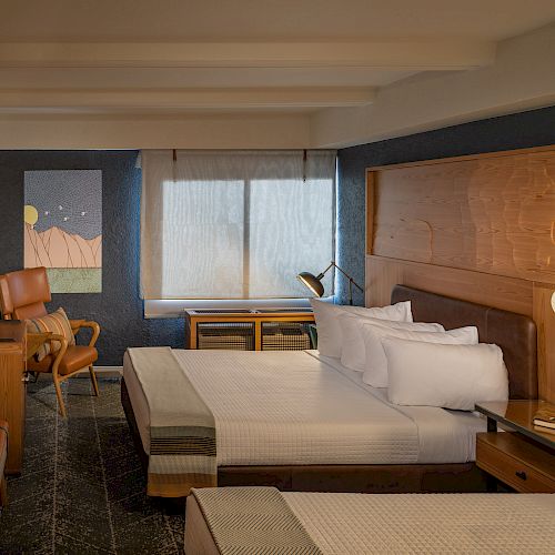 A modern hotel room with two beds, wooden furnishings, cozy seating, a desk, and wall art, illuminated by warm lighting.