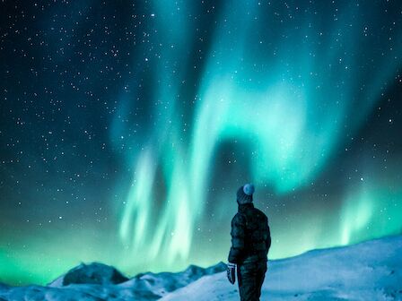 A person standing on a rock admiring the Northern Lights