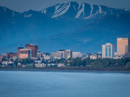 A city skyline with a backdrop of mountains and a body of water in the foreground.