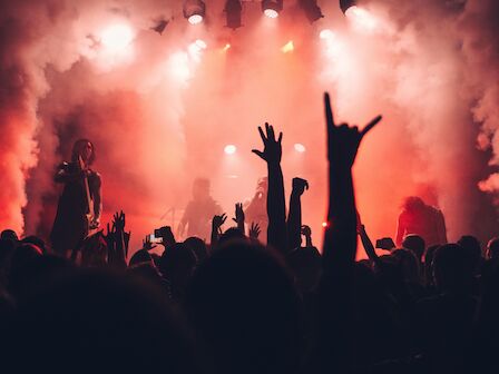 A concert scene with a crowd raising hands, red lights, and smoke effects, creating an energetic atmosphere.